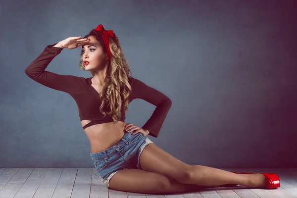 Sexig blond kvinna i jeans sundress och röda skor pin up girl retro kvinna sexig ben och en röd capitium på huvudet kryper på golvet sitter på golvet och rätar hår — Stockfoto