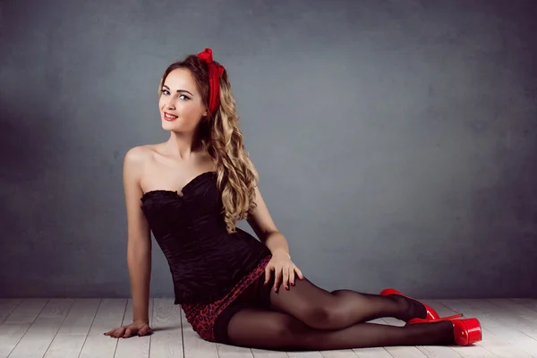 Pin up sexy hermosa mujer rubia joven maquillaje de pie en un corsé en un corsé y mini falda medias negras en tacones altos zapatos rojos costo botín rastavit pie mano hacia —  Fotos de Stock