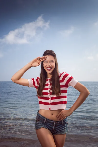 Pin up joven hermosa chica en el mar en pantalones vaqueros cortos y rayas camiseta con pelo largo rocas gafas gaviotas nubes de agua, ola, figura de sueño con gafas emociones, sonrisa con dientes, boca abierta —  Fotos de Stock