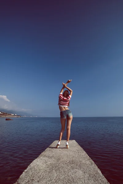 Pin up joven hermosa chica en el mar en pantalones vaqueros cortos y rayas camiseta con pelo largo rocas gafas gaviotas nubes de agua, ola, figura de sueño con gafas emociones, sonrisa con dientes, boca abierta —  Fotos de Stock