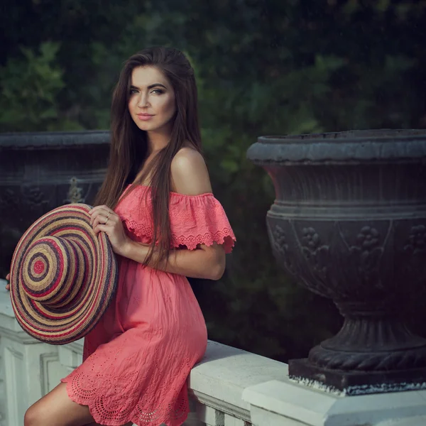 Junge schöne Mädchen in einem rosa Kleid mit einem Hut in den Händen — Stockfoto