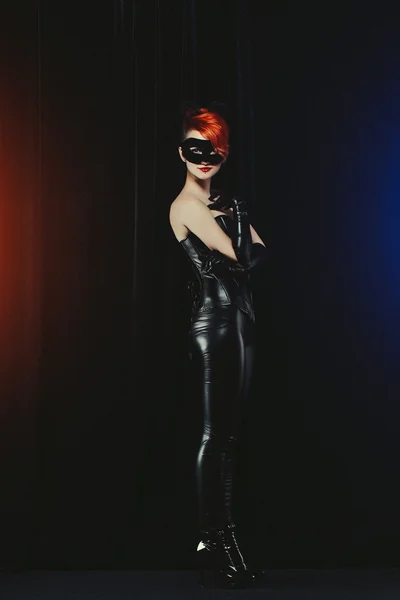 Cat woman with red hair in a leather suit with ears of a cat with a mask and makeup leather gloves — Stock Photo, Image