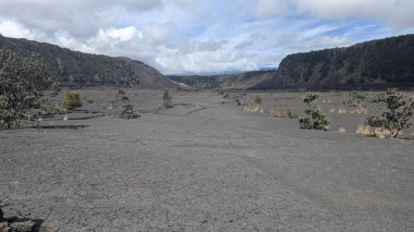 Geniş volkanik krater manzarası bulutlu gökyüzünün altında.