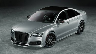 Parlak gri bir yüzeyde lüks gümüş bir sedan.