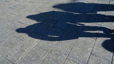 Üç kişinin gölgeleri bir taş kaldırıma dökülür..