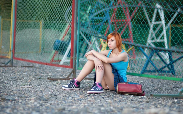 Молодая рыжая девушка в короткой юбке сидит у ограды — стоковое фото