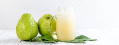 Taze meyve suyu setiyle nefis guava meyvesi. Parlak beyaz tahta masa arka planında izole edilmiş. Yakın plan..