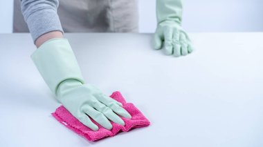 Önlüklü genç kadın temizlik yapıyor. Hastalığın yayılmasını önlemek için masa yüzeyini ıslak bezle temizliyor..
