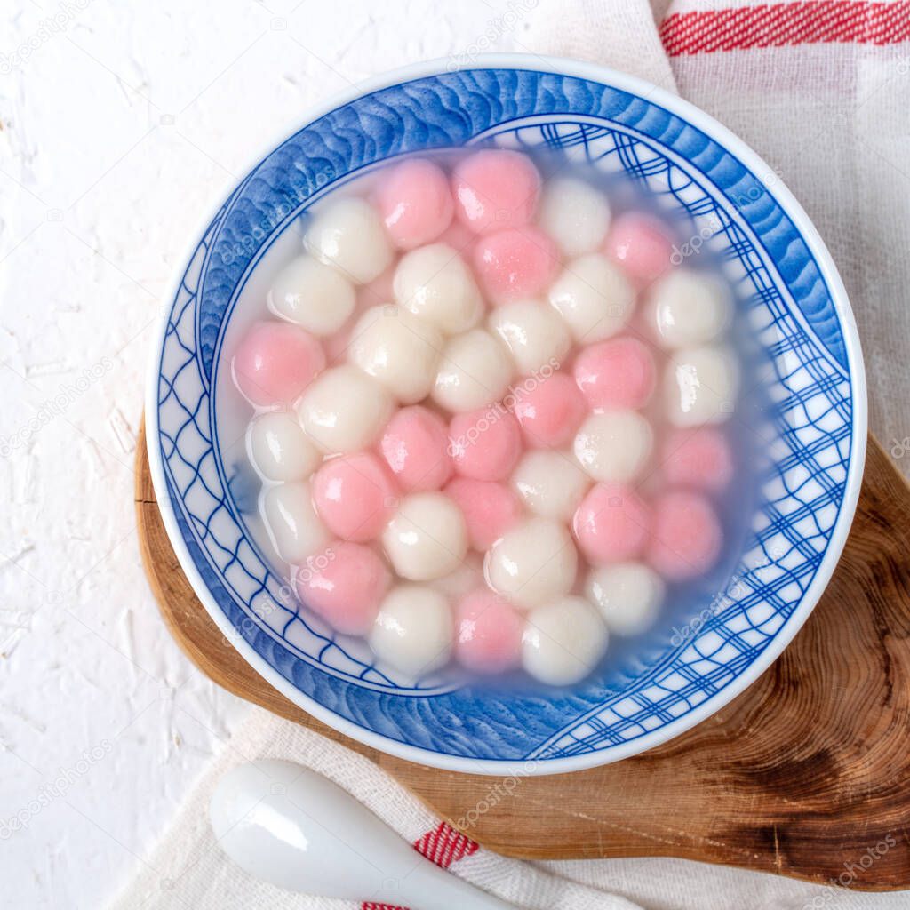 Top view of red and white tangyuan (tang yuan, glutinous rice dumpling balls) in blue bowl on white background for Winter solstice festival food.