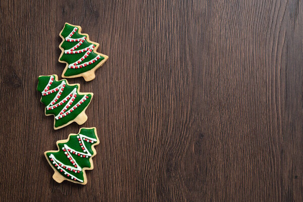 Top view of decorated Christmas tree gingerbread cookie on wooden table background with copy space, concept of holiday celebration.