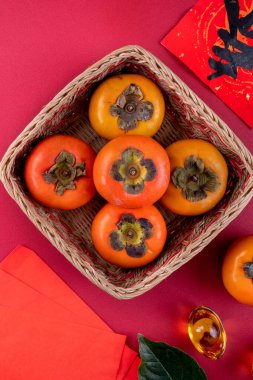 Çin 'in yeni yıl meyve tasarımı konsepti için kırmızı masa zemininde yaprakları olan taze hurma hurmalarının üst görüntüsü..