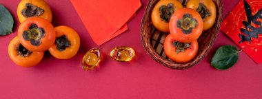 Çin 'in yeni yıl meyve tasarımı konsepti için kırmızı masa zemininde yaprakları olan taze hurma hurmalarının üst görüntüsü..