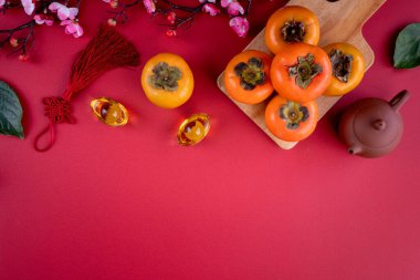 Top view of fresh sweet persimmons kaki with leaves on red table background for Chinese lunar new year fruit design concept, the word means spring is coming. clipart