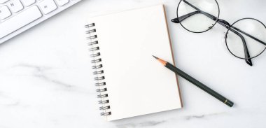 Klavye, defter, kalem, gözlük ve kahveyle birlikte parlak mermer beyaz arka planda ofis masası rahat çalışma konsepti.