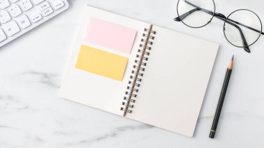 Klavye, defter, kalem, gözlük ve kahveyle birlikte parlak mermer beyaz arka planda ofis masası rahat çalışma konsepti.