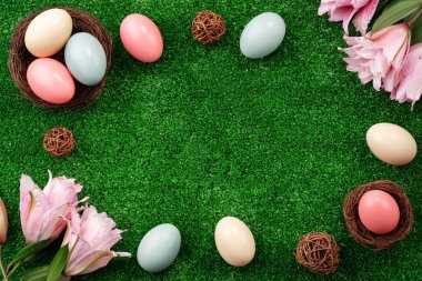 Yuvasında renkli Paskalya yumurtaları Çimen çimenlerinde pembe zambak çiçekleri.