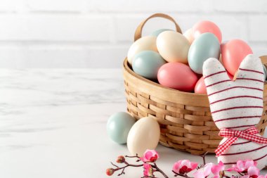Yuvadaki renkli Paskalya yumurtalarını parlak beyaz ahşap masa arkasında pembe erik çiçeğiyle kapat.