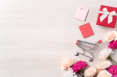 Karanfil çiçeği, bayram hediyesi fikri ve ahşap arka planda alışveriş arabasıyla Anneler Günü teması..