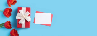 Kırmızı lale buketi ve parlak mavi masa arkaplanlı kartla anneler günü kutlama hediyesi tasarımı.