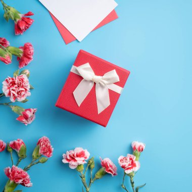 Anneler günü hediyesi. Üst görünüm tasarım tebrik kartı kavramı üzerinde kırmızı karanfil buketi olan parlak mavi masa arkaplanı