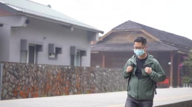 Sırt çantalı genç adam tek başına seyahat ediyor ve yürüyor. Tayvan 'da maske takmış eski bir tren istasyonuna bakıyor..