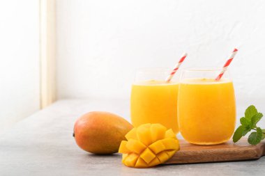 Taze mango suyu. Gri masa arkasında kağıt kamışla cam bir fincanda buzlu içecek tasarımı yakın plan..