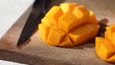 Öğlen mutfağında güneş ışığı ve yaprak gölgesi olan ahşap kesim tahtasının üzerinde doğranmış taze mango meyvesi..