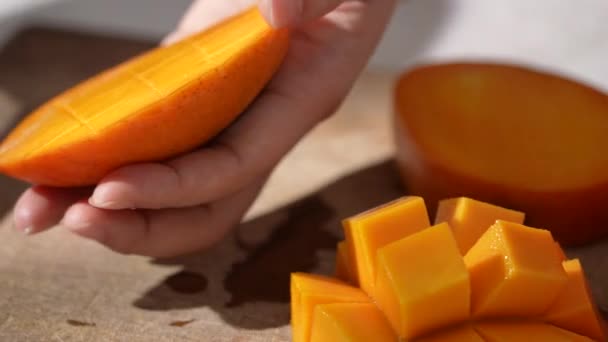 女性のスローモーションは 新鮮なマンゴーの果物を切断し 食べるための家庭用キッチンでダイスされたパルプのジューシーな側面を示しています — ストック動画