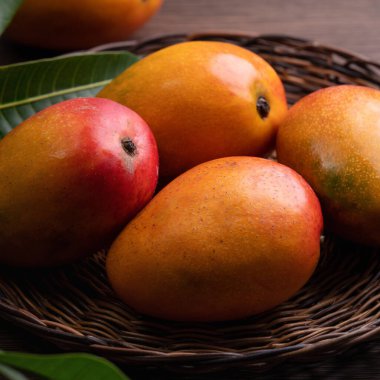 Mango. Bambu bir elek üzerinde taze olgun mango meyvesi yakın plan üzerinde koyu ahşap masa arkaplan yeşil yapraklar.