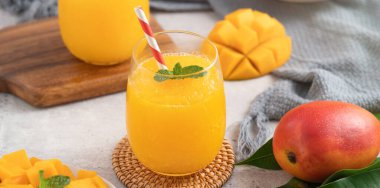 Taze nefis mango suyu. Gri masa arkasında kağıt kamışla cam bir fincanda buzlu içecek tasarımı yakın plan..