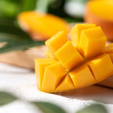 Öğlen mutfağında güneş ışığı ve yaprak gölgesi olan ahşap kesim tahtasının üzerinde doğranmış taze mango meyvesi..