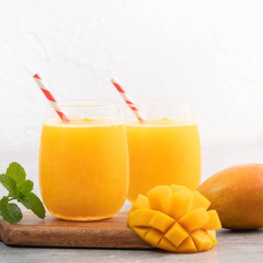 Taze nefis mango suyu. Gri masa arkasında kağıt kamışla cam bir fincanda buzlu içecek tasarımı yakın plan..
