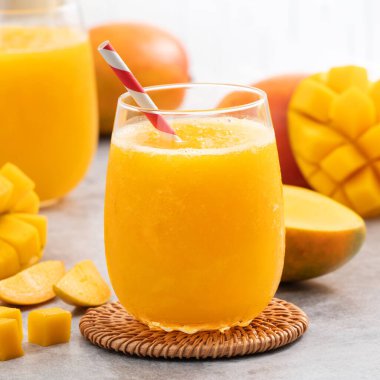 Taze nefis mango suyu. Gri masa arkasında kağıt kamışla cam bir fincanda buzlu içecek tasarımı yakın plan..