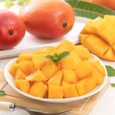 Tahta masa arkasında yaprakları olan beyaz bir tabakta doğranmış taze mango meyvesi..