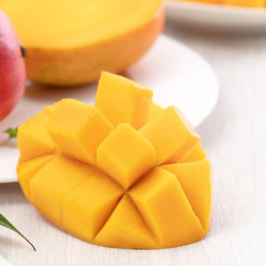 Tahta masa arkasında yaprakları olan beyaz bir tabakta doğranmış taze mango meyvesi..