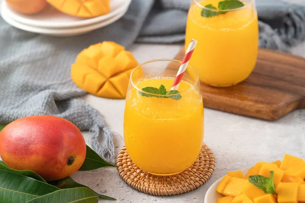 Taze nefis mango suyu. Gri masa arkasında kağıt kamışla cam bir fincanda buzlu içecek tasarımı yakın plan..