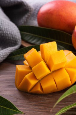 Mango. Taze olgun mango meyvelerini koyu ahşap masa zemininde yeşil yapraklarla kaplayın..