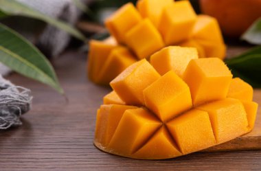 Mango. Taze olgun mango meyvelerini koyu ahşap masa zemininde yeşil yapraklarla kaplayın..