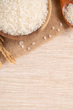 Ahşap masa arka planında kulağı olan bir kasede beyaz çiğ pirinç..