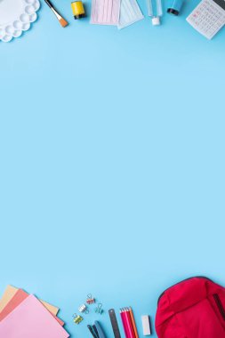 Mavi masa arkaplanının üzerinde okul kırtasiyesi olan pembe sırt çantasının üst görüntüsü, okul tasarım konseptine geri dönüş.