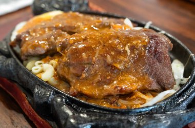 Tayvan usulü sıcak biftek, erişte, yumurta ve sos ve sıcak demir tabakta..