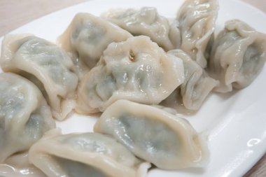 Taze, lezzetli sarımsaklı soğanlı börek, yeşil soğanlı ciaozi, ahşap masa arkasında beyaz tabakta.