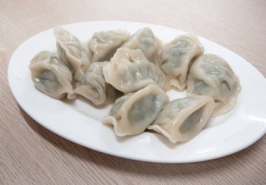 Taze, lezzetli sarımsaklı soğanlı börek, yeşil soğanlı ciaozi, ahşap masa arkasında beyaz tabakta.