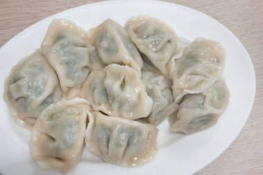 Taze, lezzetli sarımsaklı soğanlı börek, yeşil soğanlı ciaozi, ahşap masa arkasında beyaz tabakta.