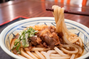 Biftek, soğan ve çıtır tempura kırıntılarıyla kaplı bir kase Japon körili udon eriştesi..