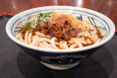 Biftek, soğan ve çıtır tempura kırıntılarıyla kaplı bir kase Japon körili udon eriştesi..