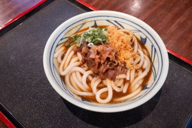 Biftek, soğan ve çıtır tempura kırıntılarıyla kaplı bir kase Japon körili udon eriştesi..