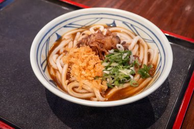 Biftek, soğan ve çıtır tempura kırıntılarıyla kaplı bir kase Japon körili udon eriştesi..