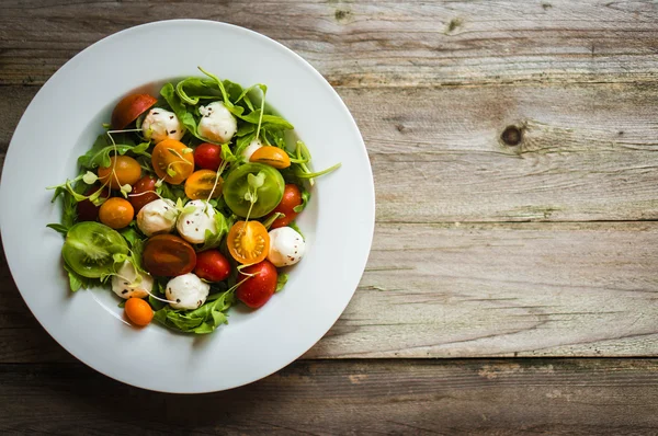 Sallad med rucola, tomater och mozarella på trä bakgrund — Stockfoto