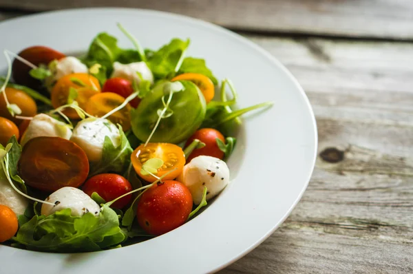 Salat mit Rucola, Tomaten und Mozarella auf Holzgrund — Stockfoto
